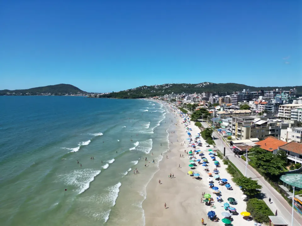 Vista aérea de uma praia de Bombinhas com a faixa de areia, o mar e a cidade