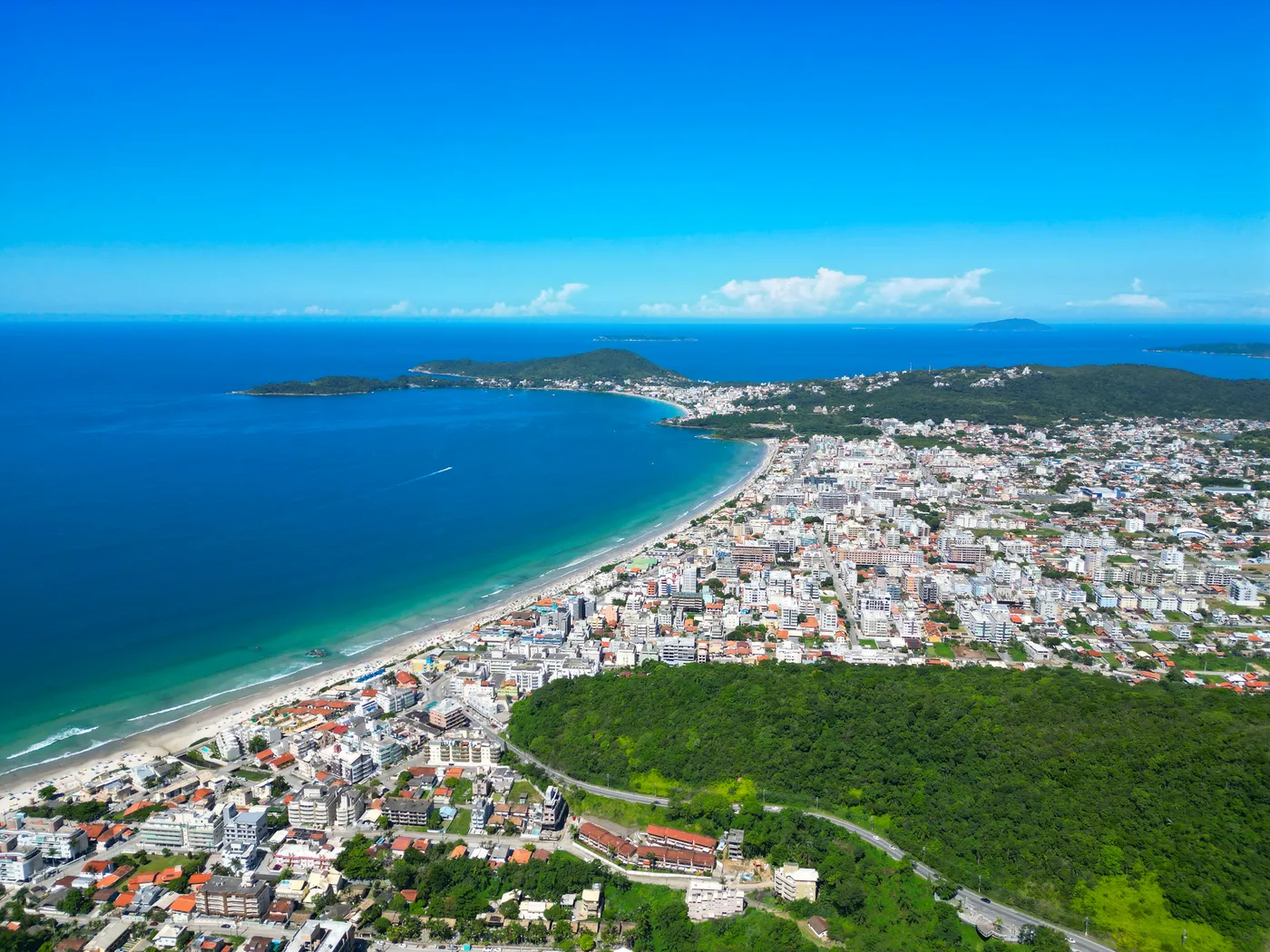 Vista aérea de Bombinhas com a península, o mar turquesa, as praias e a cidade sob o horizonte